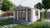 Houten tuinhuis Laula 430 x 430 x 250 cm met een wit geschilderde afwerking, geplaatst in een groene tuin met een betegeld pad ernaartoe. Het tuinhuis heeft een luifel van 100 cm en is omgeven door groenblijvende bomen en bloeiende struiken.