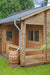 Een fraai houten tuinhuis Edelweiss (600 x 510 x 371 cm) met een houten terras, compleet met een houten balustrade. Een regenton staat strategisch geplaatst onder de dakgoot. Het tuinhuis is omgeven door een groene tuin en een blauwe lucht met enkele witte wolken.
